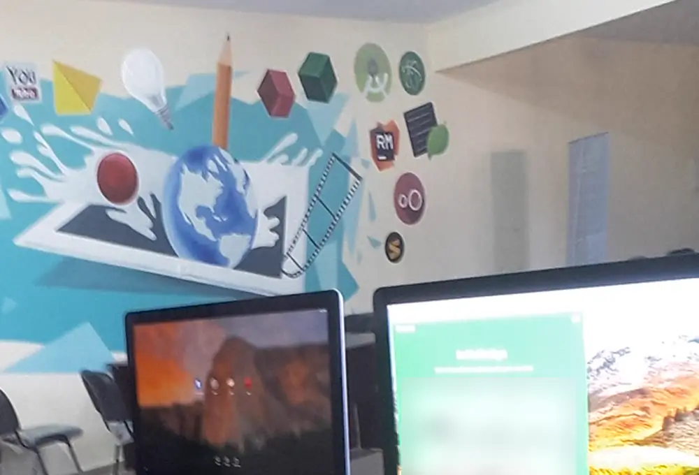 Our desks with iMacs in front of a painted tech mural at our office